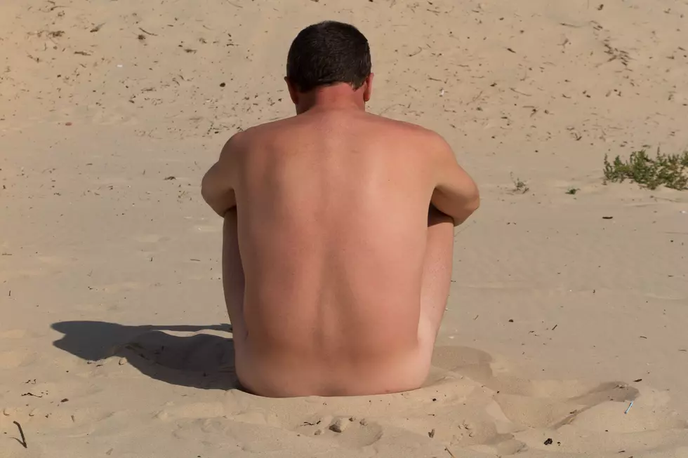 A naked man is sitting cross legged on an empty beach and meditating.